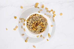 Raisin in a white bowl and are scattered on a marble table