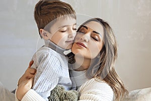 Raising Kids With Love. Cute family portrait of loving mother and little boy son hugging, isolated on beige background, close up