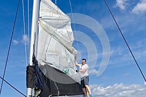 Raising the sail on a yacht. Young man captan lifting the sail of catamaran yacht during cruising