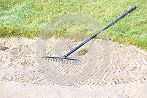 Rake in sand bunker at golf links course green for golfers