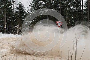Rally car drifting on the snowy winter road. Sign to give way