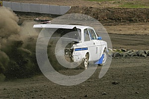 Rally Car driving with a open trunk and a gravel dust behind him