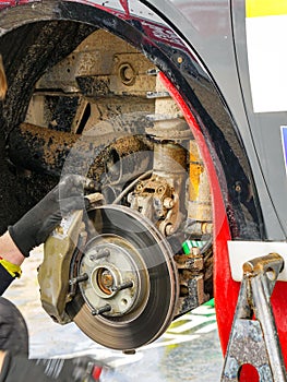 Rally car maintenance in the service park, wheel off, brake disc with caliper, muddy suspension