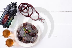 Ramadan food and drinks concept. Ramadan Lantern with arabian lamp, wood rosary, tea, dates fruit on a white wooden table