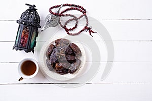 Ramadan food and drinks concept. Ramadan Lantern with arabian lamp, wood rosary, tea, dates fruit on a white wooden table