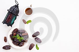 Ramadan food and drinks concept. Ramadan Lantern with tea, dates fruit, grape and Mint leaves on a white wooden table background.