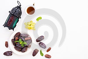 Ramadan food and drinks concept. Ramadan Lantern with tea, dates fruit, grape and Mint leaves on a white wooden table background.