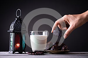 Ramadan food and drinks concept. Woman hand reaches out to a plate with date with Ramadan Lantern with arabian lamp, wood rosary,