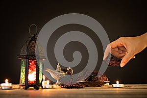 Ramadan food and drinks concept. Woman hand reaches out to a plate with date with Ramadan Lantern with arabian lamp, wood rosary,