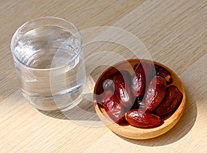 Ramadan iftar food, date fruits and glass od water on wooden table