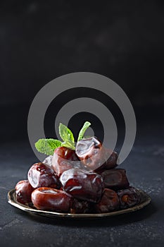 Ramadan. Iftar starts. Dates in bowl garnish mint on black background. Close up. Vertical format