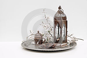 Ramadan Kareem still life. Date fruit, white flowers cup of tea and glowing Moroccan lantern on silver plate. Table
