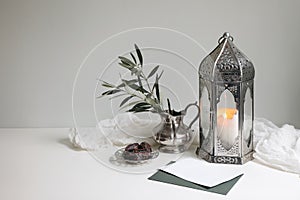 Ramadan Kareem still life. Glowing ornamental lantern. Olive tree branches in silver jug, vase.Blank vard mockup. Date