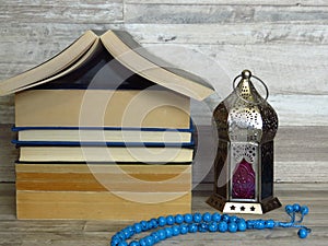 Ramadan Ramazan time celebration. A pile of home shaped old books, silver Ramadan lantern, blue turquoise chaplet, worry-beads.