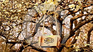 Ramadan time. Islam religion symbol. Miniature Quran in a wooden case with Islamic calligraphy on a chain on blooming