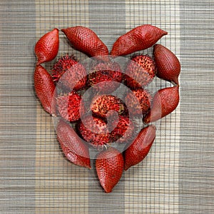 Rambutan and dragon fruits organised in heart shape on brown bamboo mat background