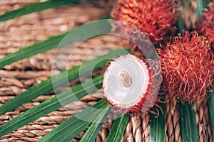 Rambutan fruits with palm leaves on rattan background. Top view. Copy space. Tropical fruit. Nephelium lappaceum. Flat lay. Exotic