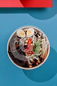 Ramen soup with eggs and udon on rose pastel color plate at blue background with sunlight and shadows, minimalism,top view