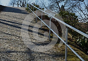Ramp with stone paving surface. railing with galvanized surface. park with a path on the slope