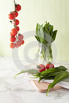 Ramsons and cherry tomatoes on marble work surface in a kitchen. Healthy food concept