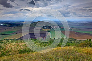 Rana Hill, in Ceske Stredohori mountain, Czech Republic. Hill with clouds. Beautiful morning landscape. Village below the hill. La