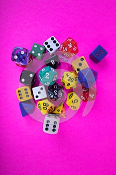 Random assorted colors and sizes of gaming dice on bright pink background