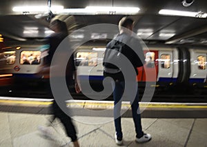 Random passenger people at the underground tube station with moving train motion blurred. London England