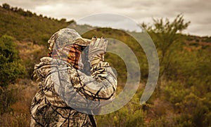 Ranger in camouflage suit and mask watches through binoculars in wooded area