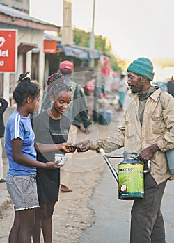 Ranohira, Madagascar - April 29, 2019:  Unknown Malagasy man selling fruit drink to two young girls on street, pouring it directly