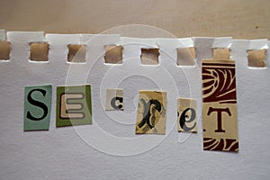 Ransom note style collage saying Secret on a sheet of white paper torn out of a notebook photo