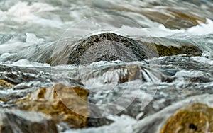 Rapid spring river flowing over rocks forming white water waves, closeup detail - abstract nature background