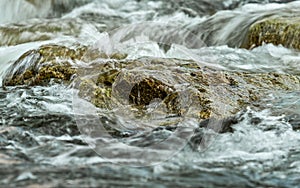 Rapid spring river flowing over rocks forming white water waves, closeup detail - abstract nature background