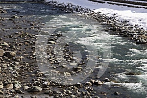 A rapids of mountain rivers with fast water and large rocky boulders. Rapid flow of a mountain river in spring, close-up