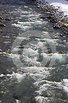 A rapids of mountain rivers with fast water and large rocky boulders. Rapid flow of a mountain river in spring, close-up