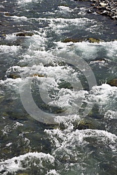 A rapids of mountain rivers with fast water and large rocky boulders. Rapid flow of a mountain river in spring, close-up