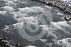 A rapids of mountain rivers with fast water and large rocky boulders. Rapid flow of a mountain river in spring, close-up