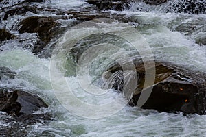 Rapids of mountain rivers with fast water and large rocky boulders. Rapid flow of a mountain river in spring, close-up