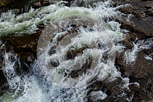 Rapids of mountain rivers with fast water and large rocky boulders. Rapid flow of a mountain river in spring, close-up