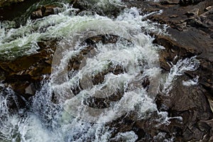 Rapids of mountain rivers with fast water and large rocky boulders. Rapid flow of a mountain river in spring, close-up