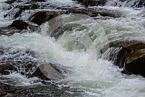 rapids of mountain rivers with fast water and large rocky boulders. Rapid flow of a mountain river in spring, close-up