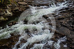 rapids of mountain rivers with fast water and large rocky boulders. Rapid flow of a mountain river in spring, close-up