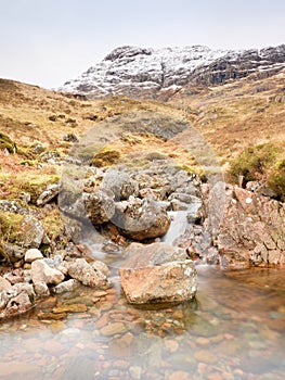 Rapids in small waterfall on stream, Higland in Scotland an early spring day. Snowy mountain peaks photo