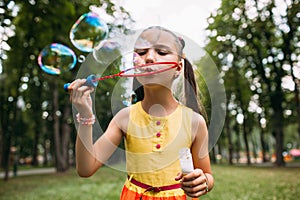 Rapt little girl blows bubbles in the park.
