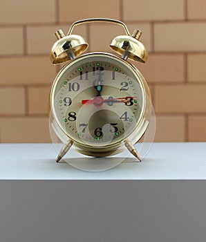 Rare copper clock with bells on a gray wooden shelf in front of brickwork background