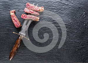 Rare medium cuts of ribeye steak on folk on gray cutting board. Top view