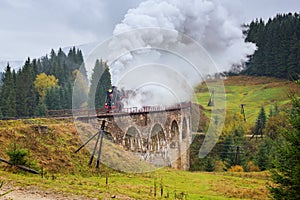 Rare steam train locomotive passing over the old viaduct in the mountains