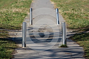 Rarely used old paved path with cracked asphalt and four broken damaged shiny metal protective poles