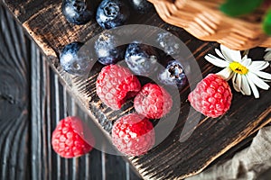 Raspberries and blueberries in a basket with chamomile and leaves on a dark background. Summer and healthy food concept