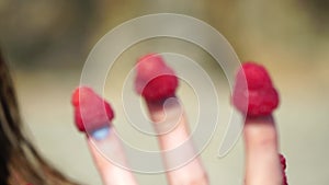 Raspberries, fingers, beach, summer. Ripe red raspberries on happy smiling lady fingertips at a beach during summer