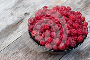 Raspberries in a glass bowl on a wooden rustic table.